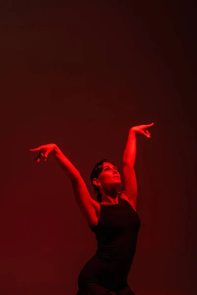 Graceful dancer in black dress performing tango on dark background with red illumination — Stock Photo
