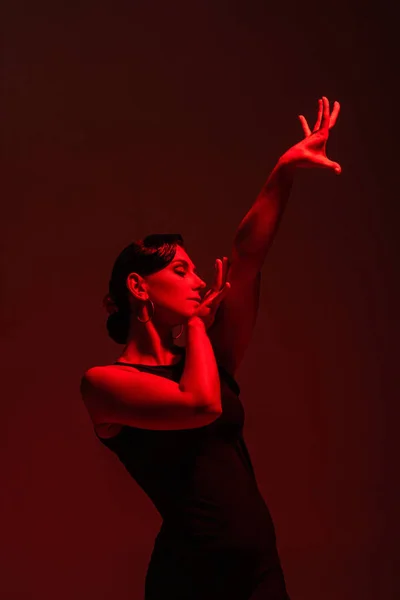 Belle danseuse en robe noire exécutant le tango sur fond sombre avec éclairage rouge — Photo de stock