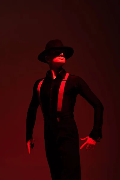 Expressive dancer in black clothing and hat performing tango on dark background with lighting — Stock Photo