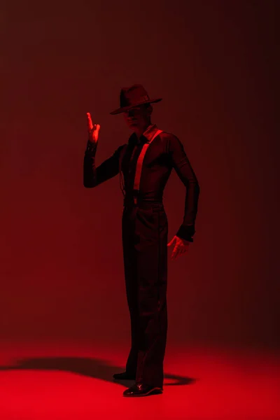 Dançarina elegante em chapéu preto realizando tango no fundo escuro com iluminação vermelha — Fotografia de Stock