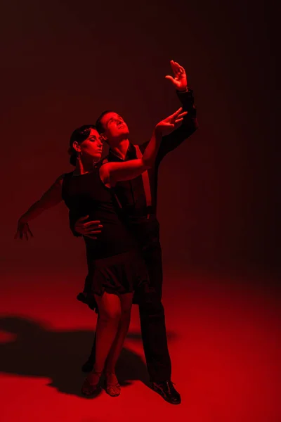 Stilvolles Tanzpaar in schwarzer Kleidung, das Tango auf dunklem Hintergrund mit roter Beleuchtung aufführt — Stockfoto