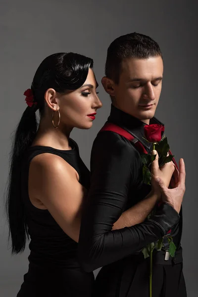 Handsome tango dancer gifting red rose to attractive partner isolated on grey — Stock Photo