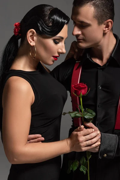 Guapo bailarín de tango regalando rosa roja a atractiva pareja aislada en gris - foto de stock