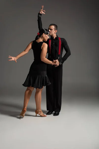 Two expressive dancers in black clothing performing tango on grey background — Stock Photo