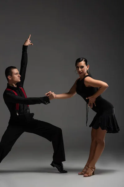 Expressive couple of dancers in black clothing performing tango on grey background — Stock Photo
