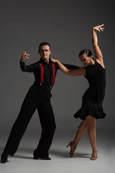 Sensual pareja de bailarines en ropa negra realizando tango sobre fondo gris - foto de stock