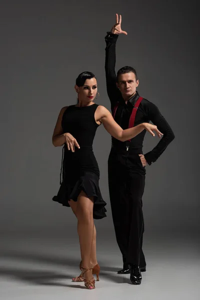 Deux danseurs expressifs en vêtements noirs exécutant le tango sur fond gris — Photo de stock