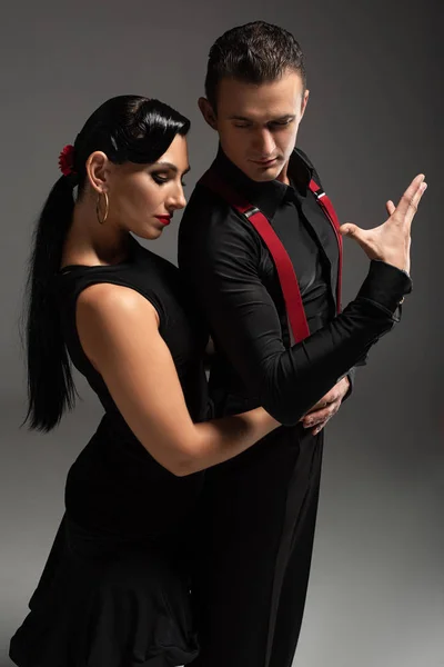 Hermosa bailarina abrazando pareja mientras realiza tango sobre fondo gris - foto de stock