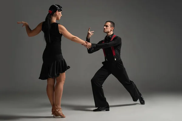 Sensual pareja de bailarines en ropa negra realizando tango sobre fondo gris - foto de stock