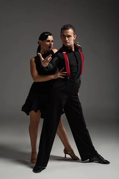 Passionate couple of dancers in black clothing performing tango on grey background — Stock Photo