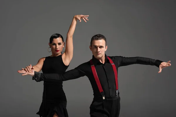 Sensual pareja de bailarines mirando a la cámara mientras realizan tango aislado en gris - foto de stock