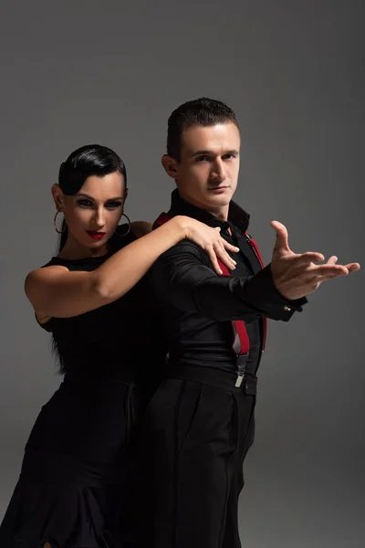 Elegante pareja de bailarines mirando a la cámara mientras realizan tango aislado en gris - foto de stock