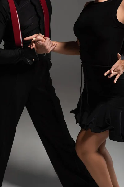 Vista recortada de bailarines en ropa negra realizando tango sobre fondo gris - foto de stock