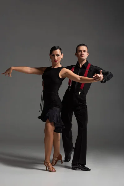 Elegant dancers in black clothing looking at camera while performing tango on grey background — Stock Photo