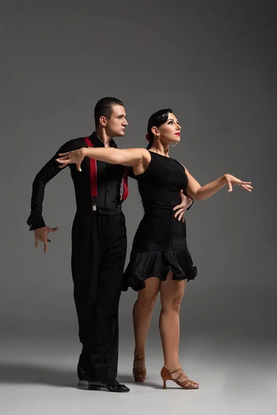 Elegante casal de dançarinos em roupas pretas realizando tango em fundo cinza — Fotografia de Stock