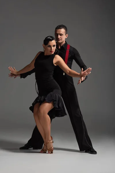 Sensual pareja de bailarines en ropa negra y elegante realizando tango sobre fondo gris - foto de stock
