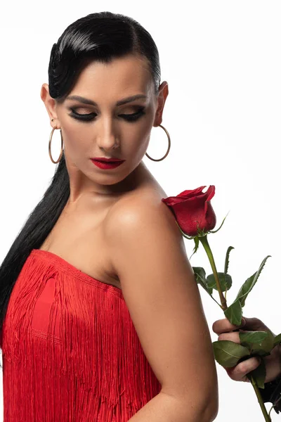 Hermosa y elegante bailarina mirando a la rosa roja en la mano de la pareja mientras realiza tango aislado en blanco - foto de stock