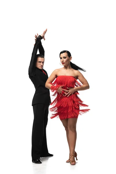 Atractiva bailarina en vestido con flecos realizando tango con elegante pareja sobre fondo blanco - foto de stock