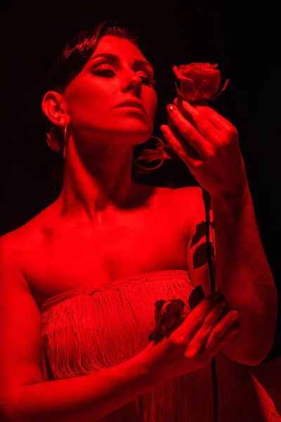 Sensual tango dancer holding red rose on dark background with red lighting — Stock Photo
