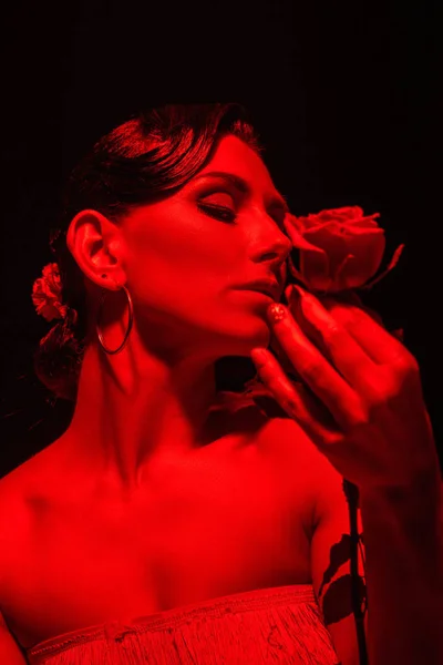 Beautiful tango dancer holding red rose on dark background with red lighting — Stock Photo