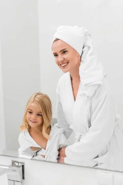 Happy mother and cute daughter looking at mirror in bathroom — Stock Photo