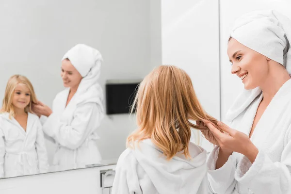 Foco seletivo da mãe feliz tocando o cabelo da filha bonito no banheiro — Fotografia de Stock