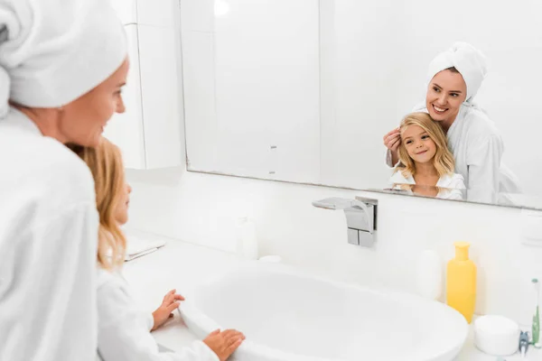 Happy kid and attractive mother looking at mirror in bathroom — Stock Photo