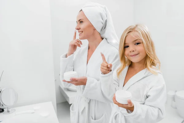 Criança alegre com nata de cara no dedo perto de mãe atraente no banheiro — Fotografia de Stock
