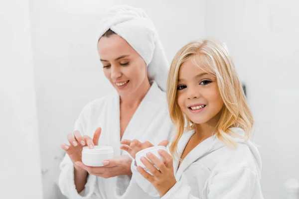 Cheerful mother and daughter holding containers with cosmetic cream — Stock Photo