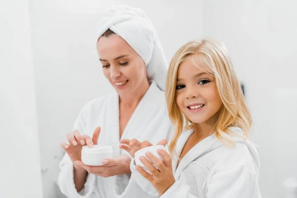 Alegre madre e hija sosteniendo contenedores con crema cosmética - foto de stock