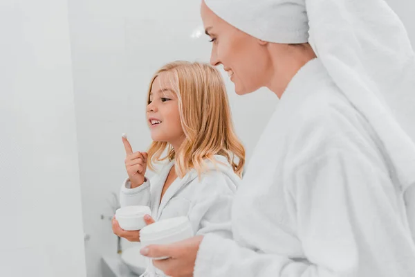 Happy mother looking at cute daughter with face cream on finger — Stock Photo