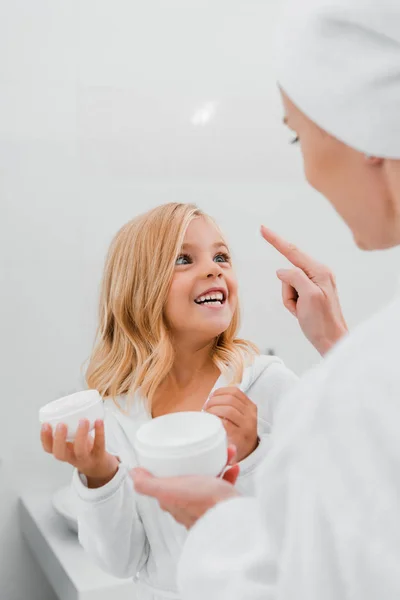 Mãe aplicando creme cosmético no rosto limpo da filha feliz — Fotografia de Stock