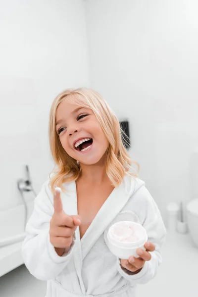 Cheerful kid with cosmetic cream in finger smiling in bathroom — Stock Photo
