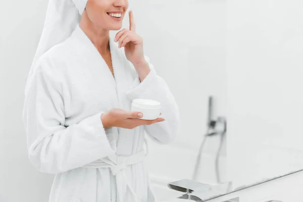 Vue recadrée de femme souriante appliquant de la crème cosmétique sur le visage propre — Photo de stock