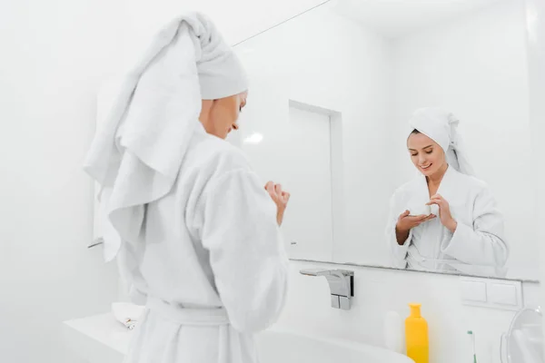 Selective focus of happy woman holding container with cosmetic cream in bathroom — Stock Photo