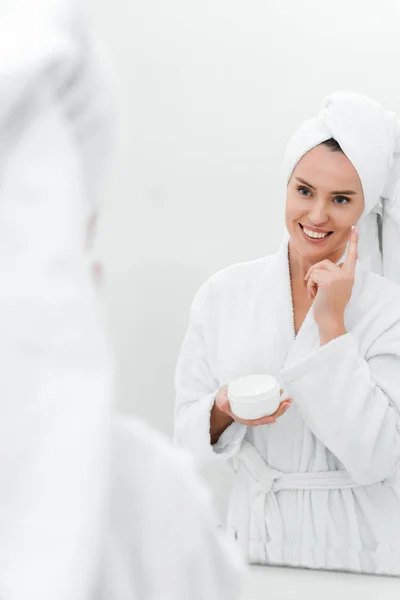 Selective focus of cheerful woman applying cosmetic cream — Stock Photo