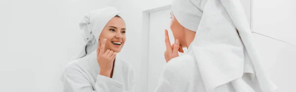 Tiro panorâmico de mulher feliz aplicando creme cosmético no rosto limpo — Fotografia de Stock