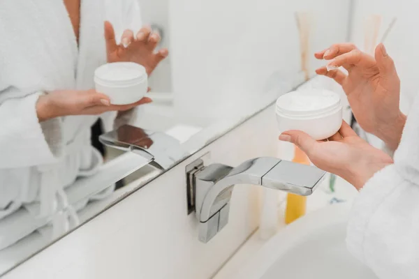 Vista cortada da mulher em roupão de banho segurando recipiente com creme facial — Fotografia de Stock