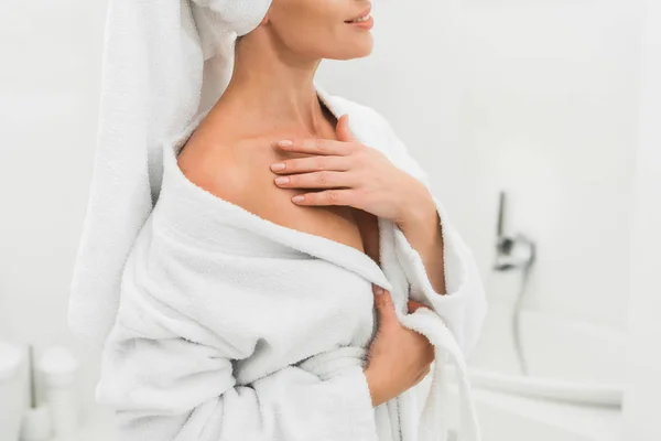 Обрезанный вид улыбающейся женщины в халате касающейся тела в ванной комнате — стоковое фото