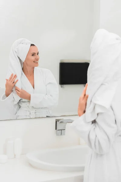 Attraktive Frau im Bademantel mit Blick auf Spiegel im Badezimmer — Stockfoto