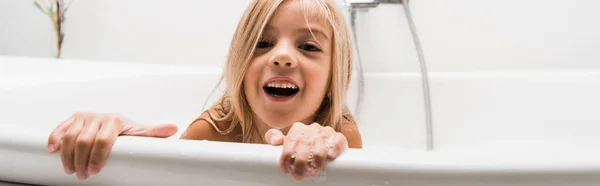 Панорамный снимок счастливого ребенка, принимающего ванну и смеющегося дома — стоковое фото
