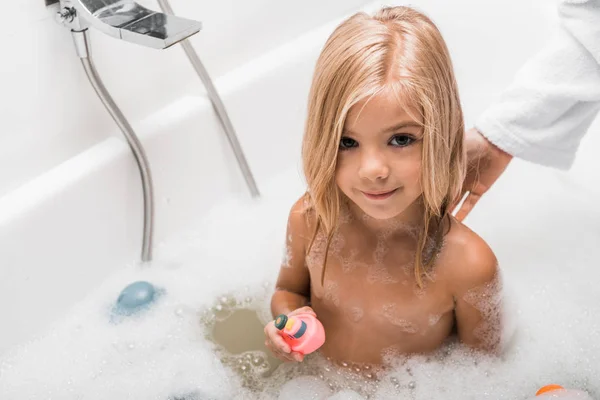 Visão aérea da criança bonita tomando banho e segurando brinquedo de borracha perto da mãe — Fotografia de Stock