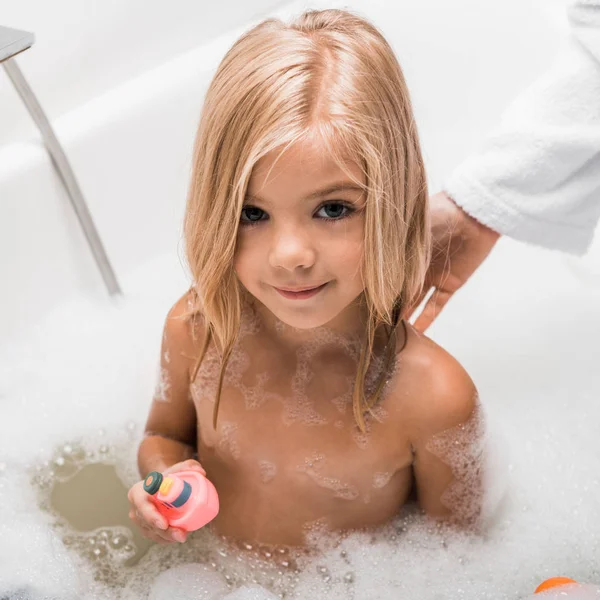 Vue aérienne de mignon enfant prenant un bain et tenant jouet en caoutchouc près de la mère — Photo de stock