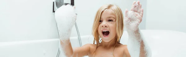 Plano panorámico de niño con la boca abierta y espuma de baño en las manos - foto de stock