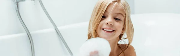 Colpo panoramico di felice bambino nudo guardando schiuma da bagno a portata di mano mentre si fa il bagno — Foto stock