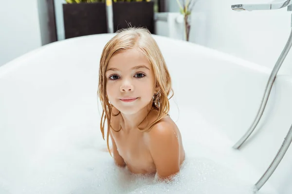 Sorridente bambino nudo che fa il bagno con schiuma da bagno a casa — Foto stock