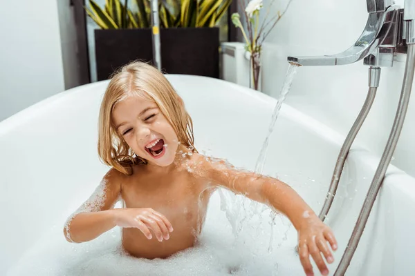 Criança nua positiva tomando banho com espuma de banho em casa — Fotografia de Stock