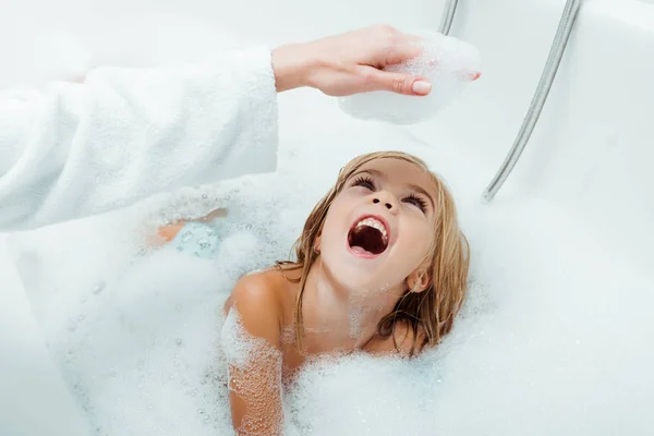 Happy kid looking at hand of mother in bath foam in bathroom — Stock Photo