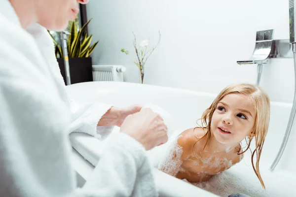 Glückliches Kind schaut Mutter beim Baden im Badezimmer an — Stockfoto