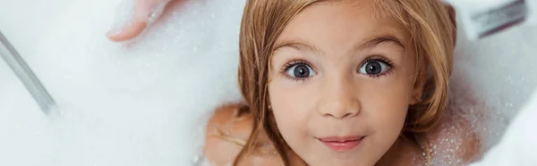 Plan panoramique d'enfant mignon prenant un bain et regardant la caméra à la maison — Photo de stock